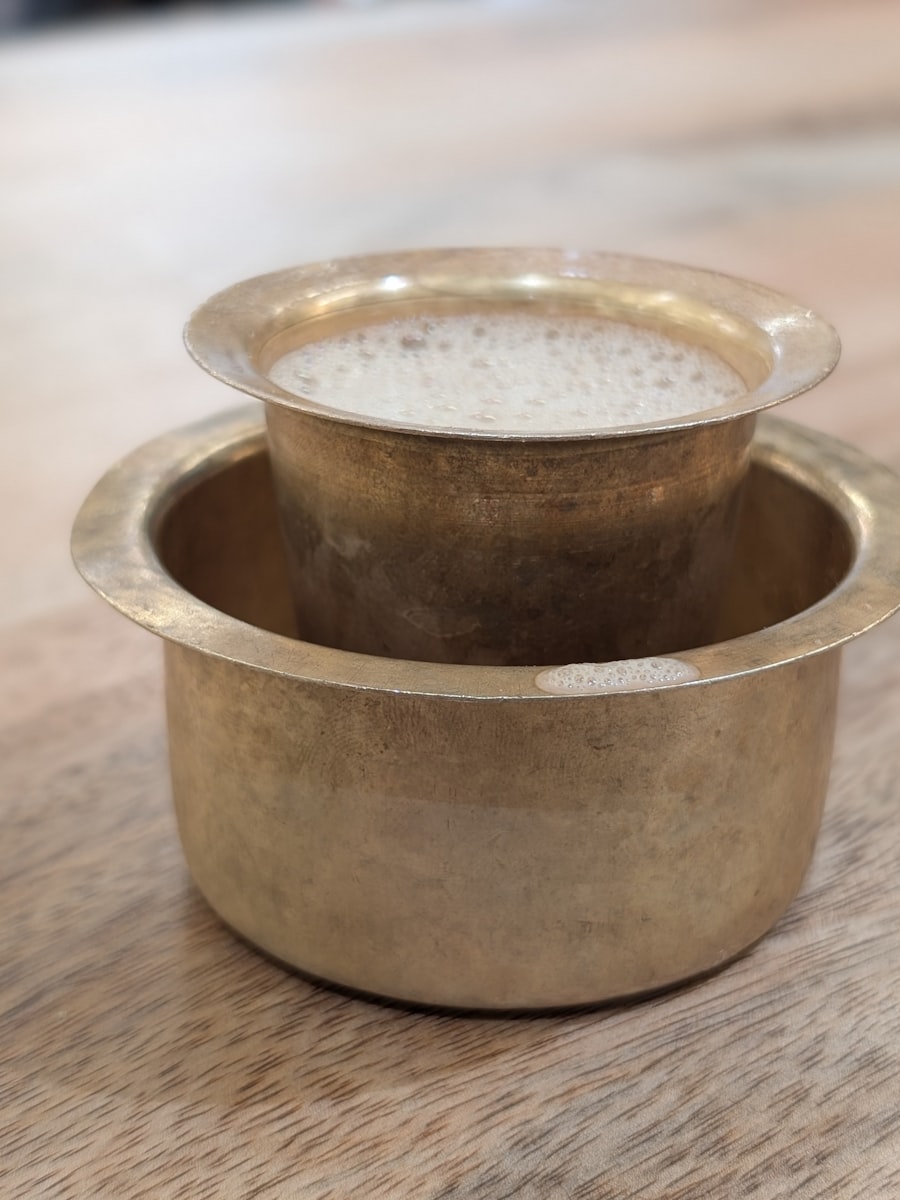 A brass davara and tumbler set with a thick collar of froth on the coffee