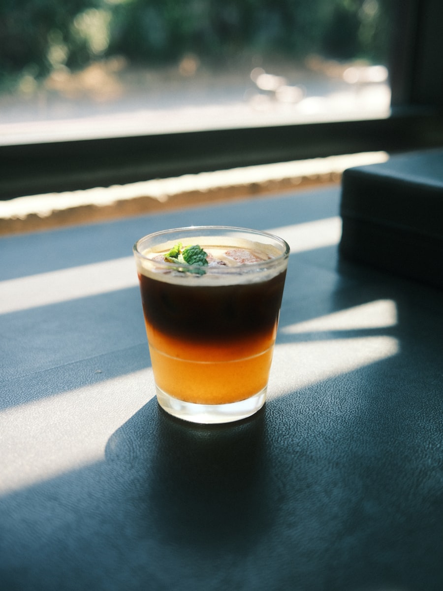 A layered coffee tonic in a short glass on a sunlit windowsill, green garnish floating on top